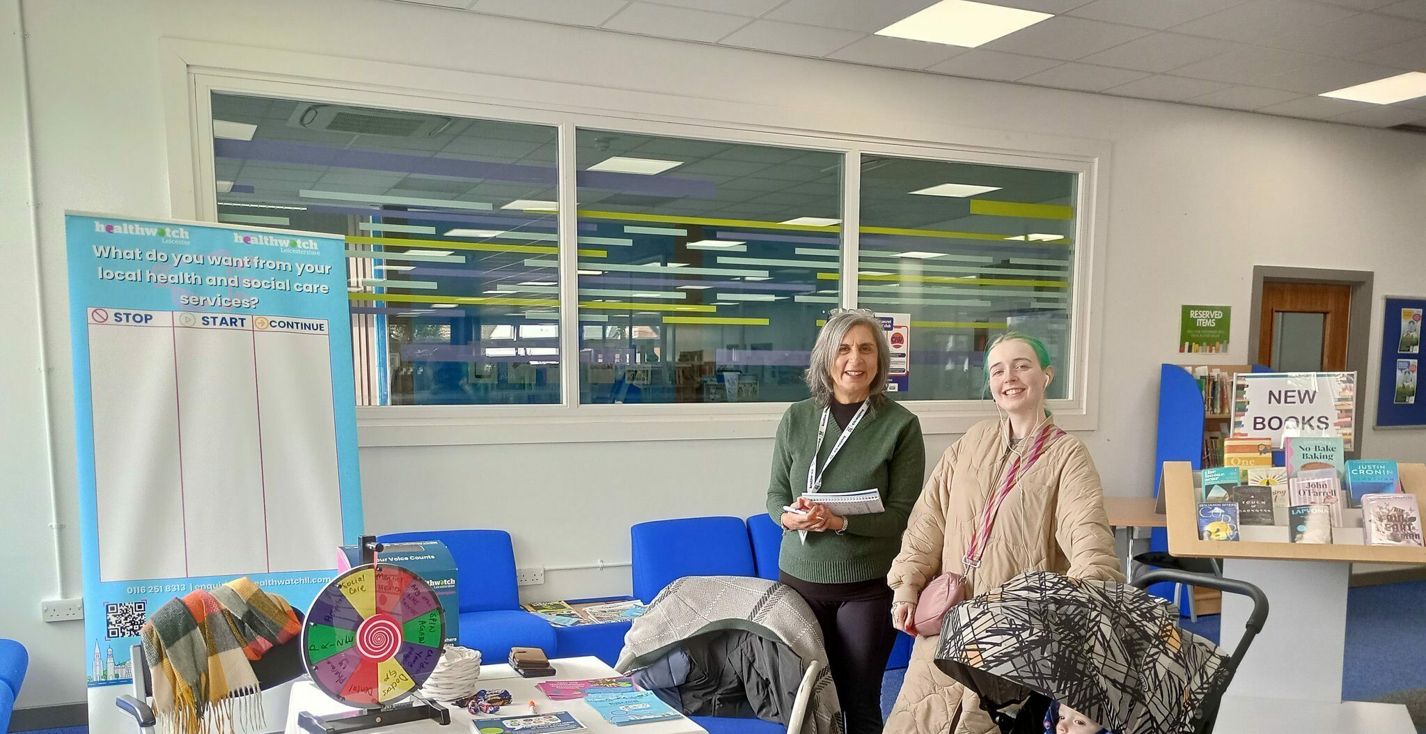 Female Healthwatch outreach officer smiling at the camera with a young mother in Wigston Library